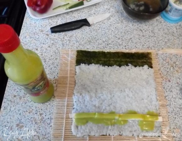 Выложить на шершавую поверхность нори рис, оставив 1–2 см листа не покрытым. Выложить бруски феты, полить соусом васаби.