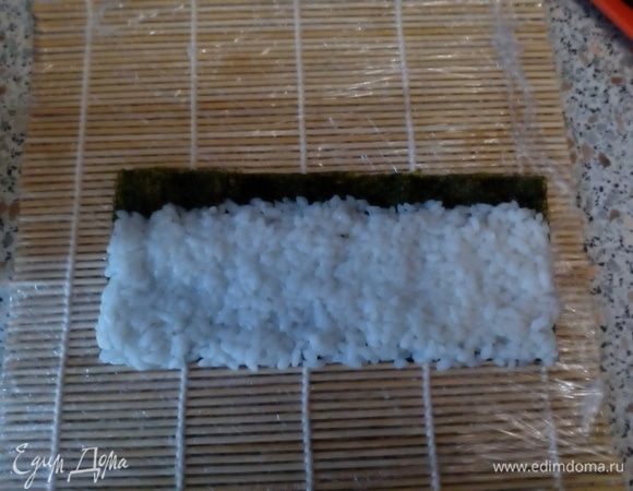 На шершавую поверхность нори выложить рис, оставит ~1 см листа не покрытым. 