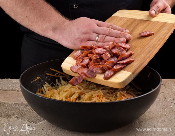 Сосиски нарежьте кубиком. Добавьте в сковороду.