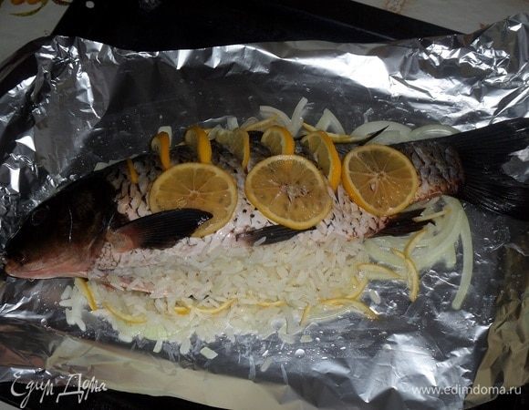 Поверх лука укладываем рыбу. Начиняем ее подготовленной рисово-луковой начинкой. В прорези вкладываем ломтики лимона. 