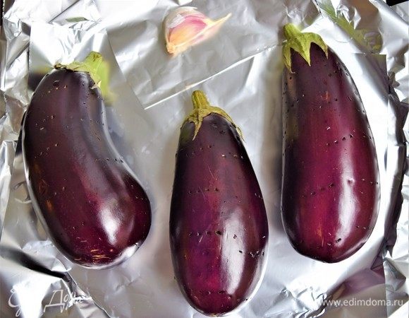 Подготовьте баклажаны и чеснок к запеканию. Баклажаны проткните вилкой со всех сторон. Зубчики чеснока заверните в фольгу. Выложите баклажаны и чеснок на лист для запекания, покрытый фольгой. (В зависимости от размера, используйте 2 или 3 баклажана. Около 700 г). Разогрейте духовку до 220°С.