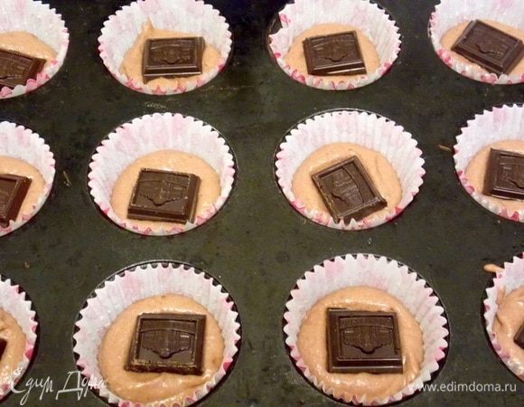 В бумажные формы для кексов положить часть теста. На нее положить кусочек шоколада.