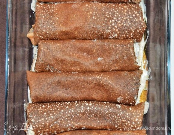 Последний шаг — запекаем нафарширанные начинкой блины под соусом. Разогрейте духовку до 190°С. Каждый блин намажьте тонким слоем баклажанной начинки и сверните, подогнув бока внутрь, чтобы начинка не вытекла при запекании. В блюдо для запекания налейте немного растительного масла, а затем соус бешамель тонким слоем. Выложите нафаршированные блины в один ряд и обильно залейте соусом бешамель, включая бока. Сверху, при желании, посыпьте сыром. Закройте блюдо фольгой и отправьте в духовку на 15 минут. Затем уберите фольгу и запекайте еще 5 минут. Блюдо готово.