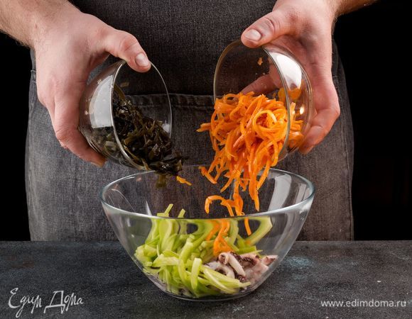 В салатнике соедините морскую капусту, морковь по-корейски, нарезанный огурец и щупальца кальмаров.
