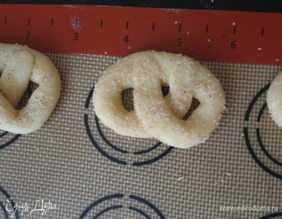 В миске смешать сахар и корицу для посыпки печенья. Каждый кренделек обмакнуть в смесь, можно прижать немного пальцами. Я пекла на силиконовом коврике, смазывать его не нужно, сразу раскладываем печенье на небольшом расстоянии друг от друга.