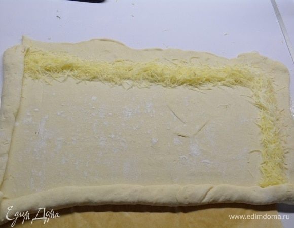 Растелить лист пекарской бумаги. На нем раскатать тесто в прямоугольный пласт. По краям насыпать тертый сыр пармезан, отступив от края чуть-чуть.