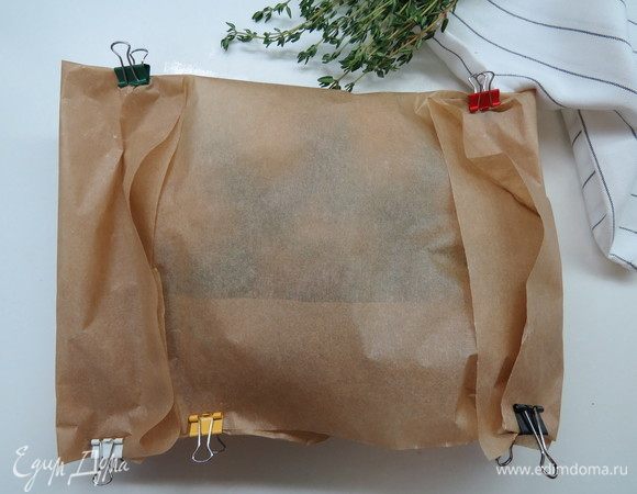 Накрыть картофель сверху свободной половиной пергамента, затем загнуть швы по бокам. Я для удобства использую канцелярские зажимы, но можно и просто сложить. Если конверт сложен не совсем герметично, это не страшно.