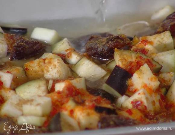 На дно жаропрочной керамической формы всыпать рис, сверху разложить кусочки баклажана, чеснок, порванные руками финики, полить все соусом, посыпать зирой и залить бульоном так, чтобы рис был полностью покрыт.