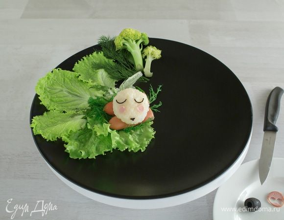 Для удобства ставим блюдо на вращающуюся подставку и начинаем творить! Сюжет нужно продумать заранее и набраться терпения:) Сначала лучше положить листья салата, на них легче передвигать персонажей. Не прикасаясь к рису руками, аккуратно перекладываем элементы из пленки на листья зелени. Глазки и носик овечки я сделала из черных оливок, ножки и щечки — из тоненькой сосики. Из инструментов использовала острый нож и кухонные ножницы.