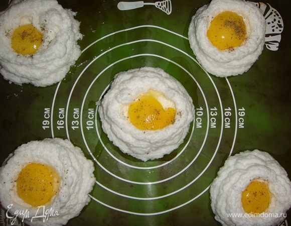 Аккуратно выложить желтки в середину каждого гнезда, посолить и поперчить по вкусу.