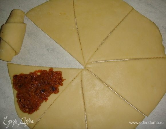 Стол слегка посыпать мукой. Раскатать одну часть теста в круг диаметром 25 см. Разрезать круг на 8 частей. На каждый треугольник выложить по одной чайной ложке начинки и распределить ее. Свернуть рогалики, начиная с широкого края. 