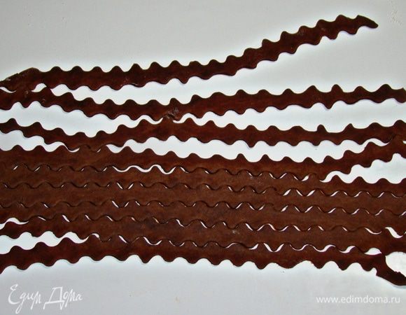 Коричневый кусочек теста раскатать тонко и нарезать фигурным ножом на полоски, шириной примерно 1 см. 