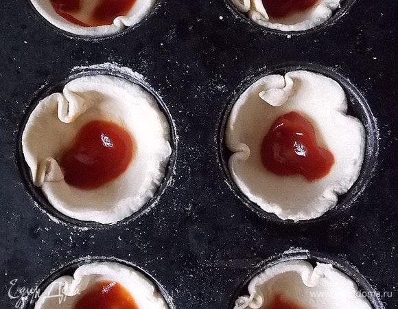 Слоеное тесто раскатать (1 лист — 250 г), не сильно, вырезать круги и кладем в смазанную маслом форму для кексов. Добавить немного кетчупа.