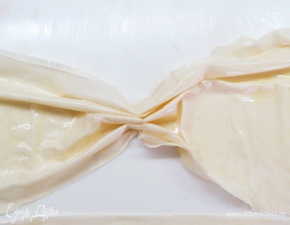 5 листов теста фило разрезать на 2 равные части. Получится 10 небольших прямоугольных листов. Берем первый лист и смазываем его растопленным сливочным масло, остальные листы кладем под влажное полотенце, чтобы не пересохли. Присобрать лист в центре, чтобы получился как бы бантик.