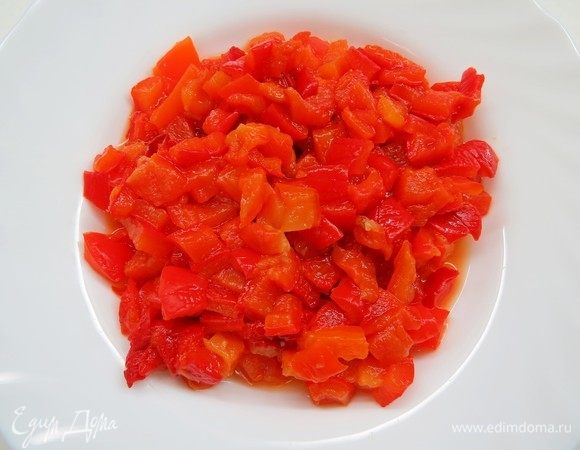 Перец вымыть, выложить на решетку и запечь в духовке, разогретой до 180°С, до мягкости и черных подпалин (около 30 минут). Переложить готовый перец в миску, закрыть крышкой и дать постоять 10–15 минут, затем очистить от кожицы, семян и перегородок. Очищенные печеный перец нарезать кубиками.