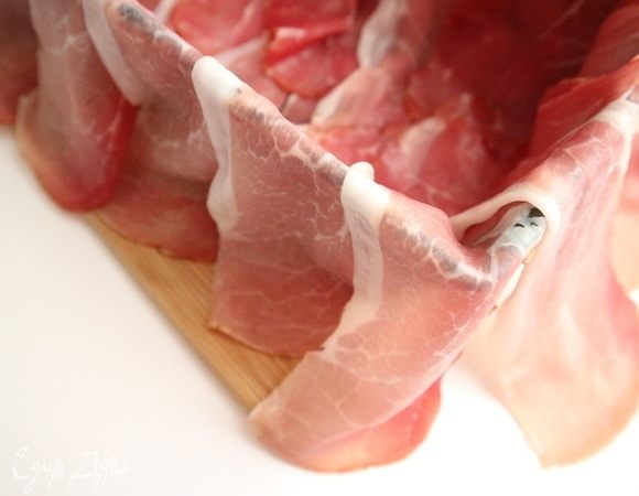 Прямоугольную форму смазать оливковым маслом, излишки удалить бумажной салфеткой, застелить сырокопченым беконом таким образом, чтобы кусочки бекона свешивались из формы, а в форме чуть-чуть заходили один кусочек на другой.