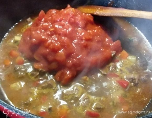 Влить воду и выложить консервированные помидоры в собственном соку, предварительно их измельчив. Воды я добавила больше, чем в оригинальном рецепте. Просто вы сами решаете, какая густота супа вас устроит. Дать закипеть, уменьшить огонь, накрыть крышкой и тушить полтора часа. До готовности мяса. 