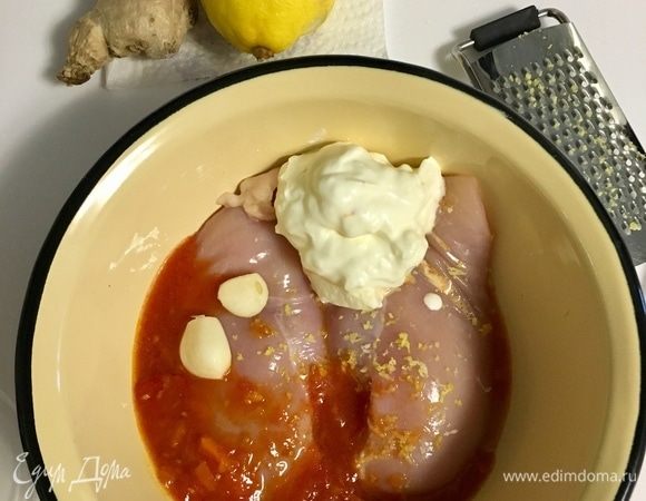Куриные грудки помыть и обсушить бумажным полотенцем. Они должны быть обязательно комнатной температуры. Будем их мариновать. Для этого к куриному филе в миску добавляем сметану, томатную пасту, натираем на терке чеснок, имбирь и лимон.