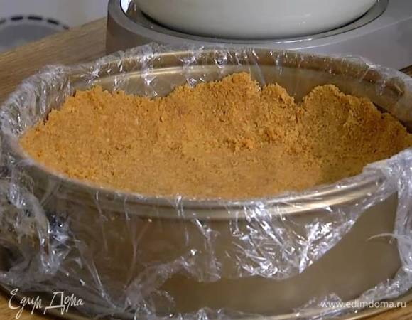 Разъемную форму для выпечки выстелить пищевой пленкой, выложить печенье и плотно утрамбовать в корж, так чтобы получились бортики, и отправить в морозильник на 10‒20 минут.