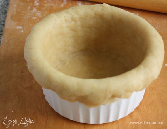 Остальное тесто раскатать в круг толщиной примерно в 5 мм и перенести его в круглую форму для выпечки с высокими бортиками и диаметром 20 см. Пальцами плотно прижать тесто ко дну и стенкам формы. Свободный край теста должен чуть свисать наружу. Форму можно брать металлическую разъемную.