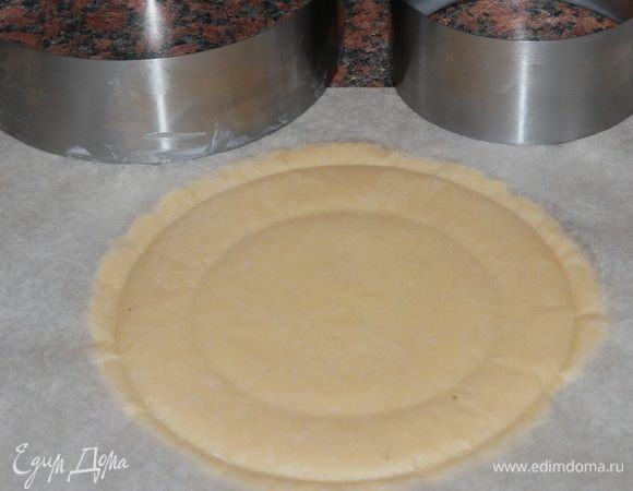 Тем временем тесто охладилось и с ним можно работать. Работать придется быстро: помним, что песочное тесто нельзя перегревать. Поэтому, если оно сильно размягчилось, отправьте его на некоторое время в морозильную камеру. А потом снова продолжайте работать. Я готовила несколько тартов разного диаметра. У меня было два тарта по 16 см, один тарт 18 см, два тарта 10 см. Как раз на все это использовала все тесто. Отрезаем кусок теста, выкладываем его между двумя листами пергамента и раскатываем в круг толщиной 3 мм. Почаще, при раскатке, переворачивайте тесто в пергаменте, чтобы равномерно раскатать и не дать ему быстро нагреться. Каждый раз, когда переворачиваете, отрывайте пергамент от теста. Таким образом вы никогда не пропустите то время, когда тесто критично нагрелось: пергамент начнет рвать тесто. Затем намечаем кольцом размер будущего тарта: осторожно надавливаем (не продавливаем) через пергамент кольцом, размер которого соответствует диаметру будущего тарта и потом кольцом, диаметр которого на 2 см больше. Потому как бортики будут высотой 2 см. Затем снимаем верхний пергамент, обрезаем излишки теста, быстро переворачиваем тесто, снимаем второй пергамент и опускаем тесто в кольцо. Внутреннюю стенку кольца предварительно смазываем маслом.