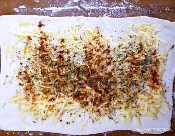 Делаем слоеные сырные плетенки. Пласт слоеного бездрожжевого теста раскатываем в прямоугольник. Посыпаем сыром, паприкой и сушеным укропом. Проходимся скалкой по начинке, так она не будет рассыпаться.