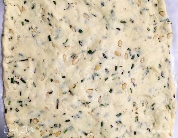 В тесто ввести остывшие загорелые кедровые орешки. Мелко порубить листики розмарина и ввести в тесто. Щепотку семян фенхеля немного растереть прямо пальцами и также отправить в тесто. Из теста прямо на бумаге для выпечки раскатать прямоугольный пласт толщиной 0,5 см.