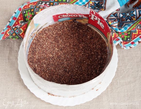 На блюдо установить сервировочное кольцо. Его можно сделать самим из картонной коробочки. Мое (диаметр 23 см) служит уже довольно долго. Внутреннюю часть кольца обернуть бумагой для выпечки или пищевой пленкой. Выложить на дно ореховую массу, распределяя равномерно и уплотняя ее рукой или толкушкой. Убрать пока в холодильник.