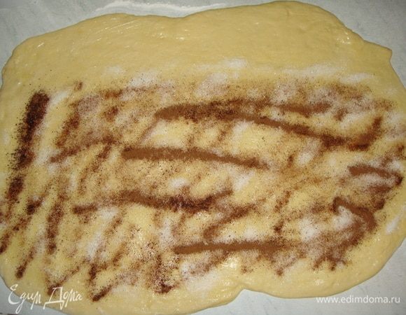 Выложить тесто на посыпанный мукой стол, раскатать тесто в прямоугольник. Смазать растопленным сливочным маслом, посыпать сахаром и корицей, оставив один край по длинной стороне нетронутым. Сворачиваем тесто в рулет, разрезаем на небольшие рулетики.