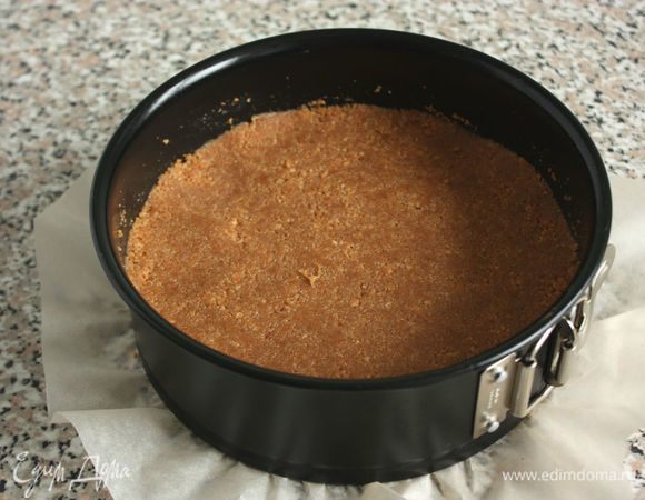 На дно разъемной формы положить бумагу для выпечки, затем надеть кольцо, бортики смазать жиром. Полученную смесь выложить в подготовленную форму и тщательно утрамбовать.