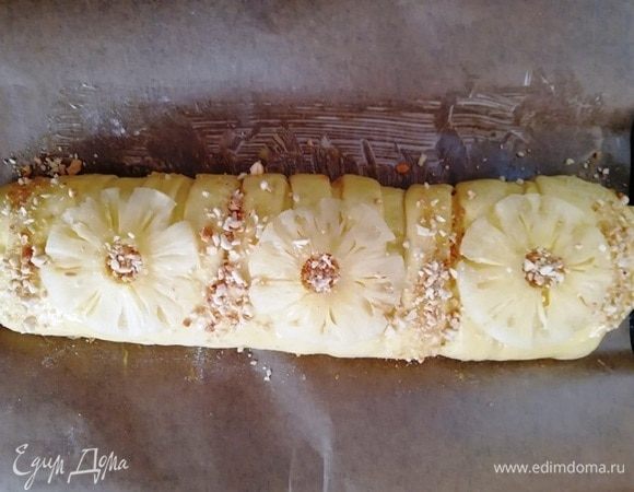 Смажьте рулет взбитым яйцом и украсьте кольцами ананаса и арахисом.