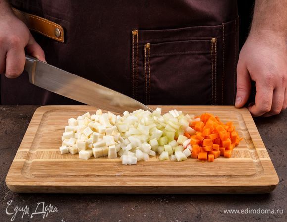 Очистите репчатый лук, сельдерей, корень сельдерея, морковь и нарежьте кубиками. В сотейнике с толстым дном разогрейте 4 ст. л. оливкового масла и обжарьте лук до прозрачности. Морковь и корень сельдерея добавьте в сотейник и томите все вместе 5 минут.