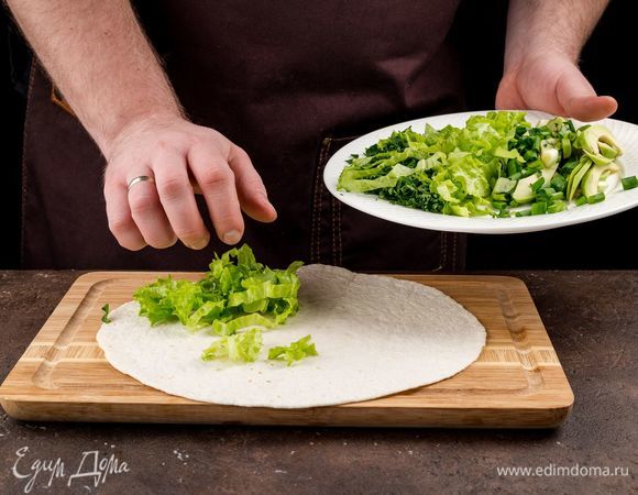 Приступаем к сборке кесадильи. Тортилью предварительно подогрейте на сковороде или в микроволновке. Положите тортилью на доску. На лепешку выложите зелень.