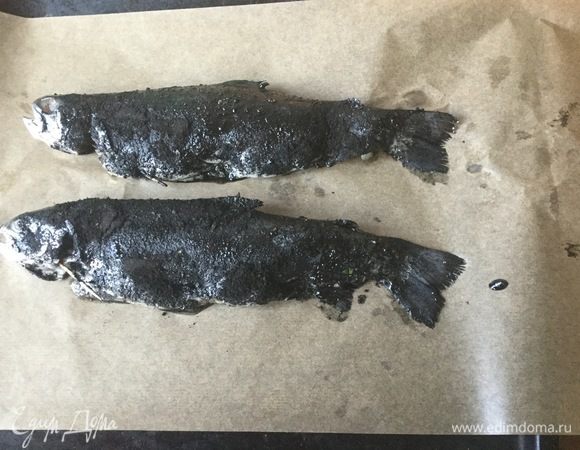 Посыпаем золой, кладем на пергамент и закрываем пергаментом. Выпекаем 30 минут при 180°С. За 10 минут до готовности, раскрываем рыбу.