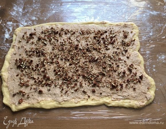 Посыпьте рабочую поверхность мукой (я застелила пищевой пленкой), раскатайте готовое тесто в пласт примерно 40*25 см. Сверху распределите сахарно-коричную смесь и орешки.