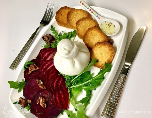 На блюдо выложить подушку из руколы. Сверху маринованную свеклу. Теперь  запеченую свеклу вместе с грецкими орехами. Сверху распределить оставшуюся половину заправки. Подсушенный загорелый хлебушек. И  король нашего завтрака — сыр буррата.