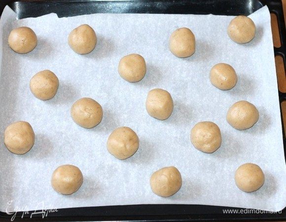 Застелить противень пекарской бумагой и выложить шарики на расстоянии друг от друга. В серединку печенья положить по 1 обжаренному орешку. Выпекать печенье в заранее разогретой до 180°С духовке, около 15 минут или до золотистого цвета. 
