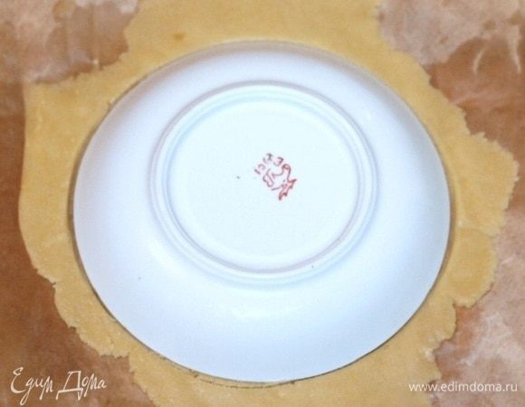 Раскатываем каждую часть теста между листами пергамента до толщины в 3 мм. Вырезаем при помощи чайного блюдца круг и переносим его при помощи скалки в формочку.
