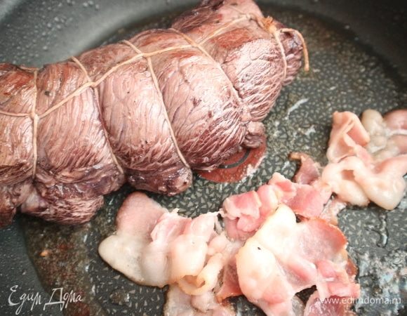 Поджарить мясо со всех сторон на раскаленной сковороде с добавлением оливкового масла и бекона. Разогреть  духовку до температуры 180°С.