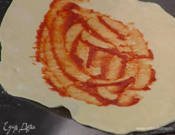 Рабочую поверхность присыпать оставшейся мукой, раскатать из отдохнувшего теста две тонкие овальные лепешки, смазать их оставшейся томатной пастой и уложить каждую на противень.