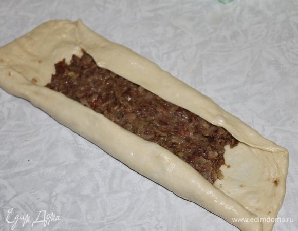 Разделите тесто на 3 части. Раскатайте каждый кусочек в овал толщиною 3 мм. Выложите по 2 столовые ложки начинки, подверните дважды внутрь края теста, формируя лодочку. Концы валиков соедините вместе и перекрутите дважды вокруг оси или хорошо слепите.