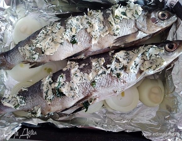 Духовку разогреть до 200°С. Рыбу обсушить салфетками. 
Надрезы и брюшко заполнить ароматным маслом. На фольгу, смазанную растительным маслом, поместить нарезанный кольцами лук, сверху уложить рыбку. 
