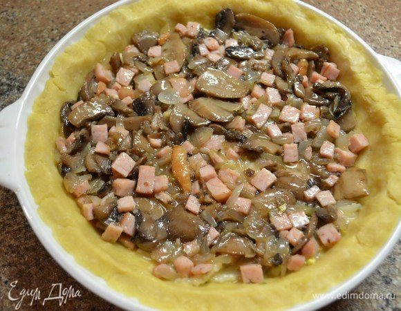 На сливочном масле обжариваем нарезанный полукольцами репчатый лук, карбонад нарезаем кубиками. Добавляем карбонад к луку и обжариваем со всех сторон. Грибы обжариваем почти до готовности на другой сковороде. Затем добавляем грибы к карбонаду и луку, хорошо перемешиваем. Укладываем начинку на тесто, разравниваем ее.