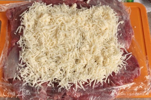 Натереть на мелкой терке твердый сыр (50 г), можно заменить на полутвердый. Выложить натертый сыр сверху на отбитое мясо, оставляя небольшие запасы для подворотов.