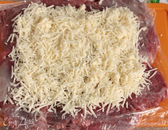 Натереть на мелкой терке твердый сыр (50 г), можно заменить на полутвердый. Выложить натертый сыр сверху на отбитое мясо, оставляя небольшие запасы для подворотов.