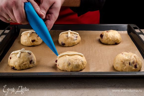 Нарисуйте на булочках кресты кондитерским мешком. Выпекайте булочки 30 минут при температуре 200°С.