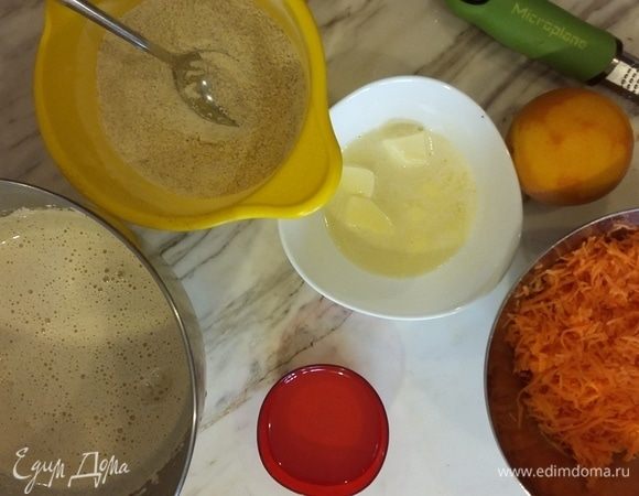Приготовим бисквит. Взбить яйца с сахаром до пышной пены. Перемешать сухие ингредиенты и аккуратно добавить в яйца. Добавить масло, затем — мелко тертую морковь и цедру. 