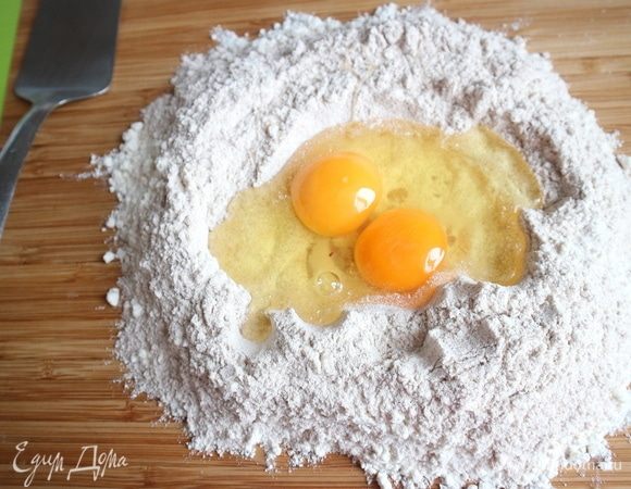 Смешать два вида муки, сделать «колодец» из муки на рабочей поверхности, разбить туда куриные яйца, сначала два яйца, здесь яйца среднего размера. Перемешать немного, можно с помощью вилки, я пользовалась металлической лопаткой.
