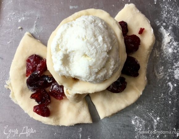 Теперь делаем так. Берем пальчиками кончики треугольничка, растягиваем вокруг творожной сердцевинки и соединяем концы с противоположной стороны. А на два других треугольничка кладем по горстке клюквы. И также берем второй треугольничек за уголки, растягиваем в стороны и защипываем с противоположной стороны. То же самое с третьим треугольничком.