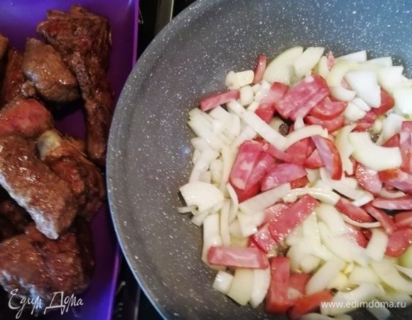 Выкладываем из сковороды говядину и на вытопившемся жире обжариваем лук и колбасу. 